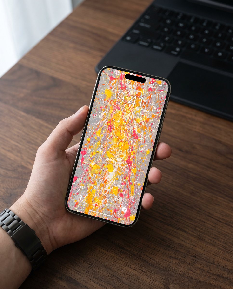 Splatter wallpaper on an iPhone held above a walnut desk
